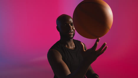 Studioporträtaufnahme-Eines-Männlichen-Basketballspielers,-Der-Vor-Rosa-Und-Blau-Beleuchtetem-Hintergrund-Einen-Ball-Auf-Dem-Finger-Dreht-1